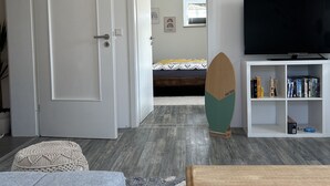 Ein modernes Wohnzimmer mit grauem Sofa, einem Holztisch, einem Fernseher und einem Bücherregal.