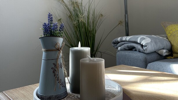 Ein Zimmer mit einem runden Tisch, einer Blumenvase, einer Kerze und dekorativen Tellern an der Wand.