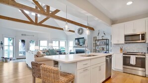 Une cuisine moderne avec des meubles blancs, un grand îlot central, des appareils en acier inoxydable et un plafond en bois.