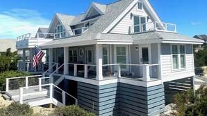 Une maison située sur la côte, dotée d’un balcon, d’un drapeau et offrant une vue sur la plage.