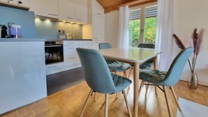 Una cocina moderna con armarios blancos, una isla central y un comedor con sillas color esmeralda.