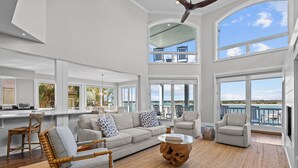 A spacious living area with a high ceiling, large windows, and a view of the ocean.