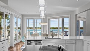 A modern kitchen with large windows, a view of the sea, and a dining area with chairs.