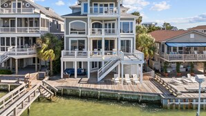A multi-story beachfront property with balconies, a wooden deck, and a dock.