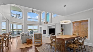 A spacious living area with a high ceiling, large windows, a dining table, and a cozy seating arrangement.