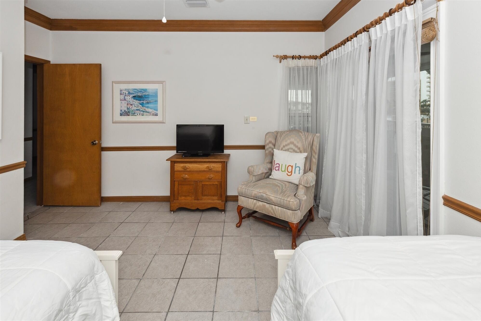A hotel room with a wooden cabinet, a television, a cushioned armchair, and a bed.