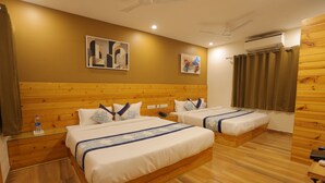 A hotel room with two beds, wooden headboard, a ceiling fan, an air conditioning unit, and artwork on the walls.