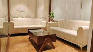A modern living room with two cream-colored sofas, a glass coffee table, and a potted plant.