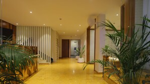 A modern hotel hallway with a polished yellow floor, wooden paneling, and potted plants.