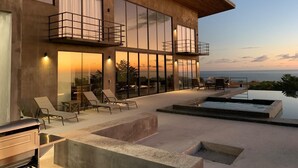 Une maison moderne à deux étages, dotée de grandes baies vitrées, d’un espace extérieur aménagé et d’une piscine.