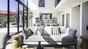 Un salon moderne avec un canapé gris, des tables d’appoint en bois et une vue sur l’extérieur grâce à de grandes fenêtres.