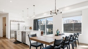 A modern kitchen with a central island, white cabinetry, and a large dining table with chairs.