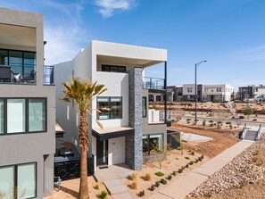 A modern residential building with a balcony, a stone column, and a well-maintained garden with shrubs and a palm tree. - A Sapphire Sunset 5 Bedroom Townhouse (St. George)