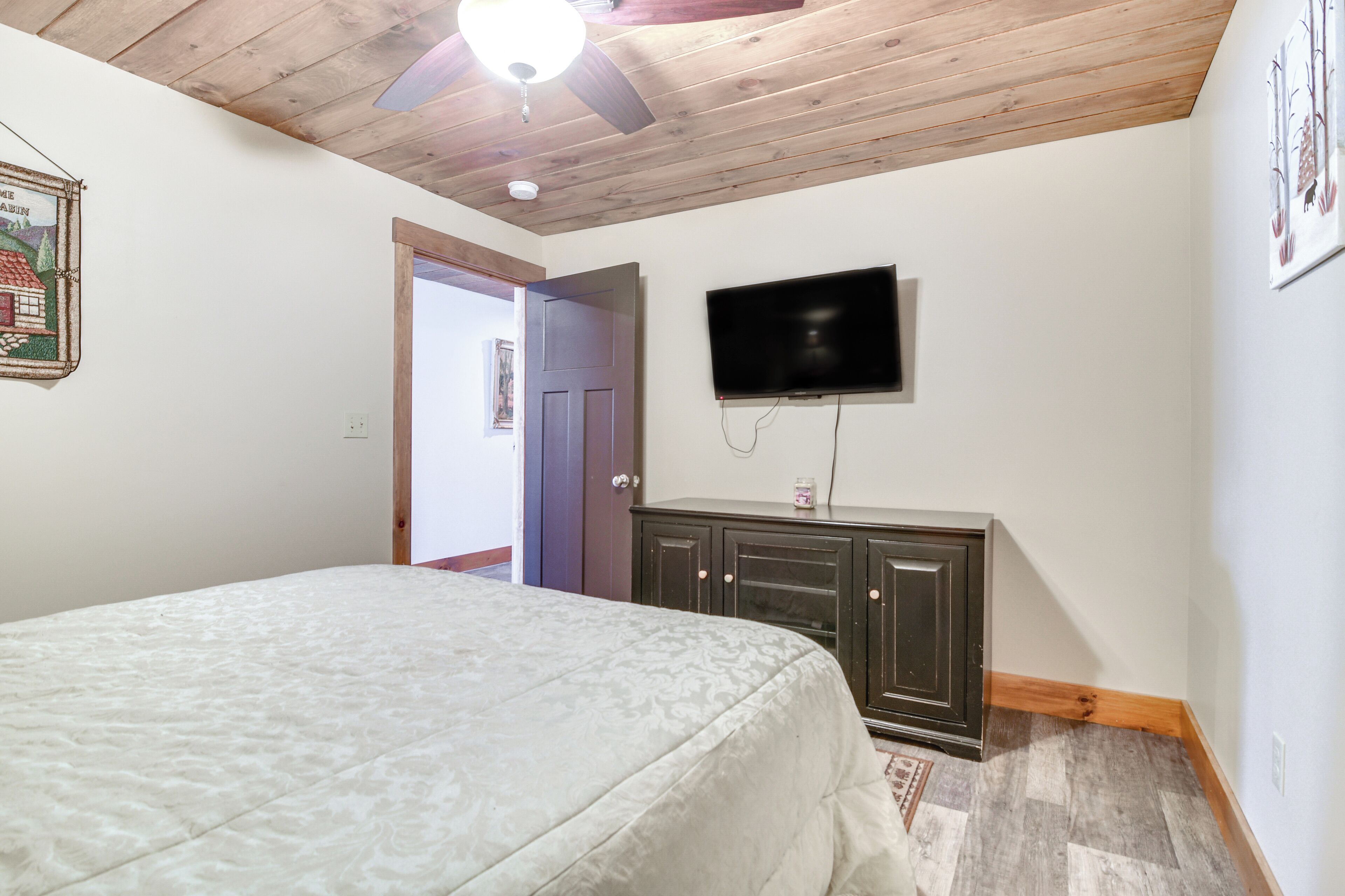 A bedroom with a bed, a ceiling fan, a television, and a door leading to another room.