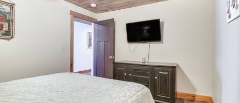 A bedroom with a bed, a ceiling fan, a television, and a door leading to another room.