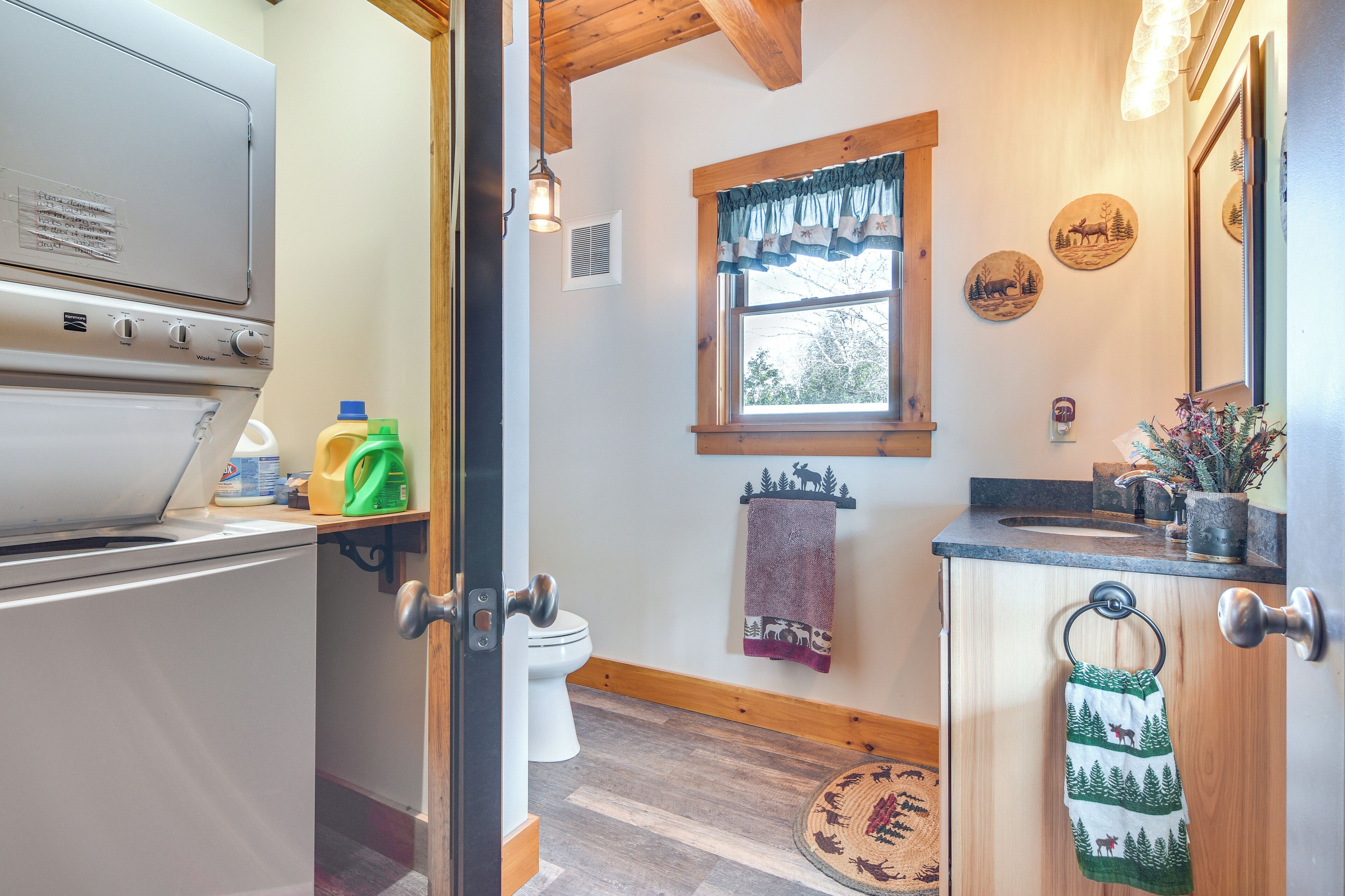 A compact kitchen with a built-in washer, a window with a curtain, and a wooden ceiling.