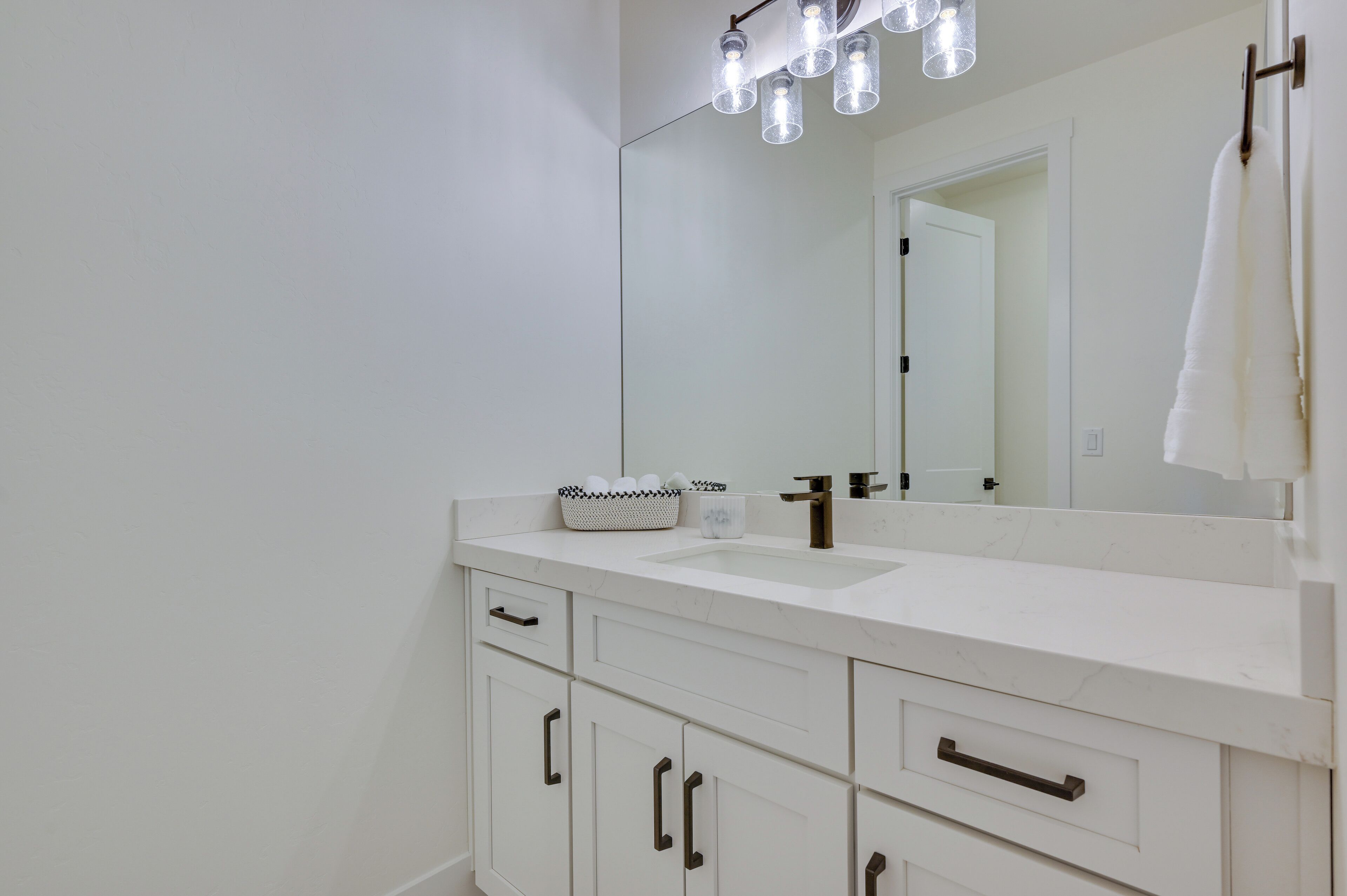 A modern bathroom with a white vanity, a large mirror, and a light fixture above the mirror.