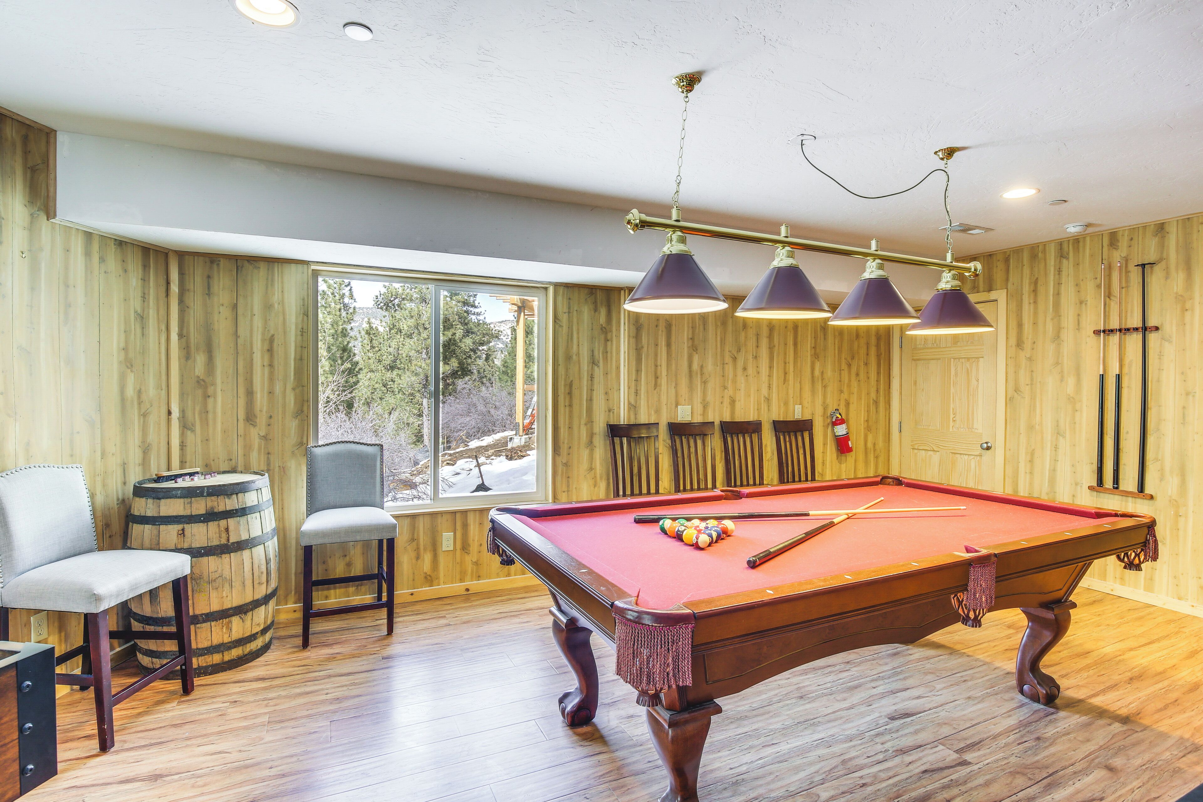 A pool table with a red felt surface, surrounded by wooden walls and a large window.