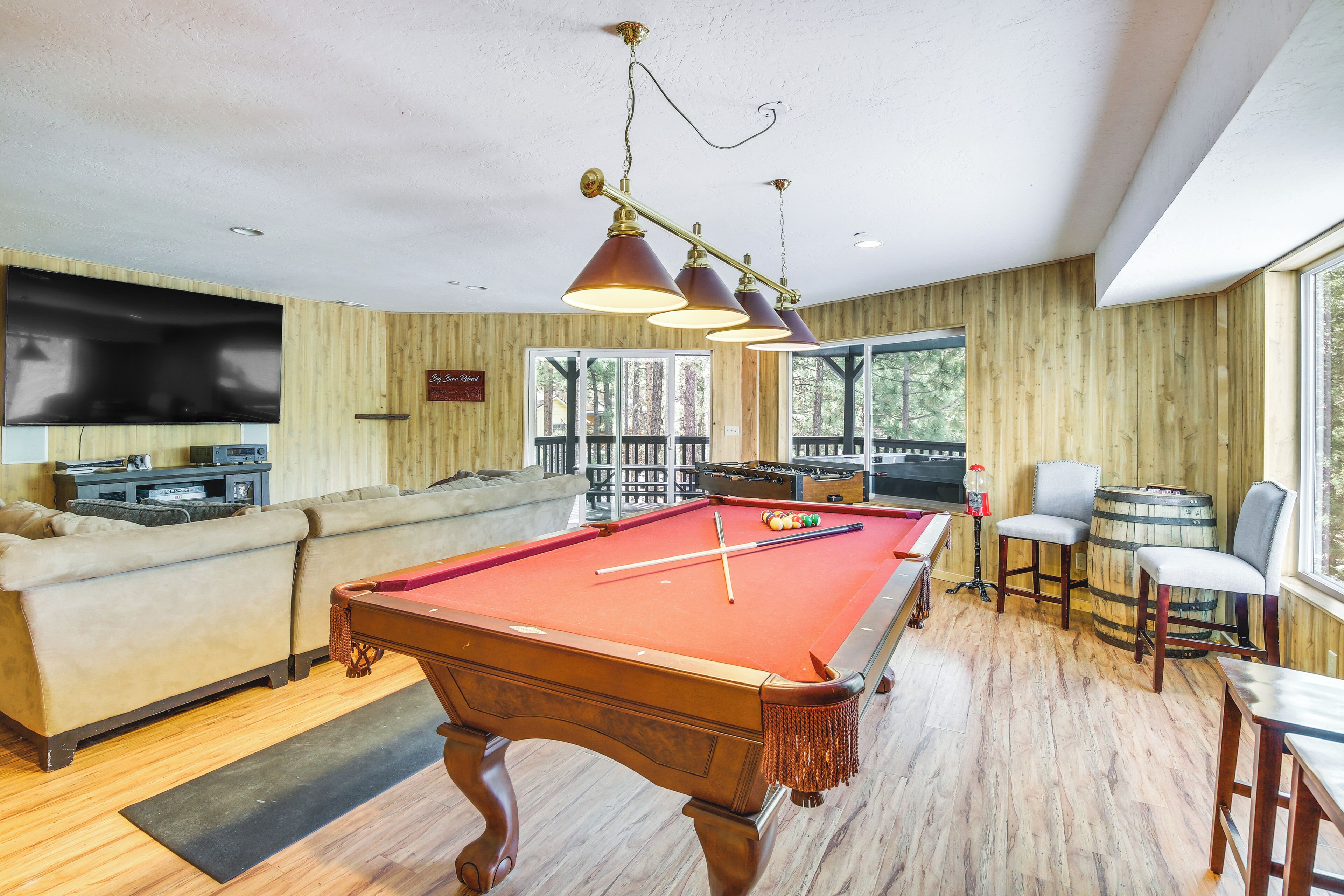 A pool table in a room with wooden walls, a sofa, and a television.