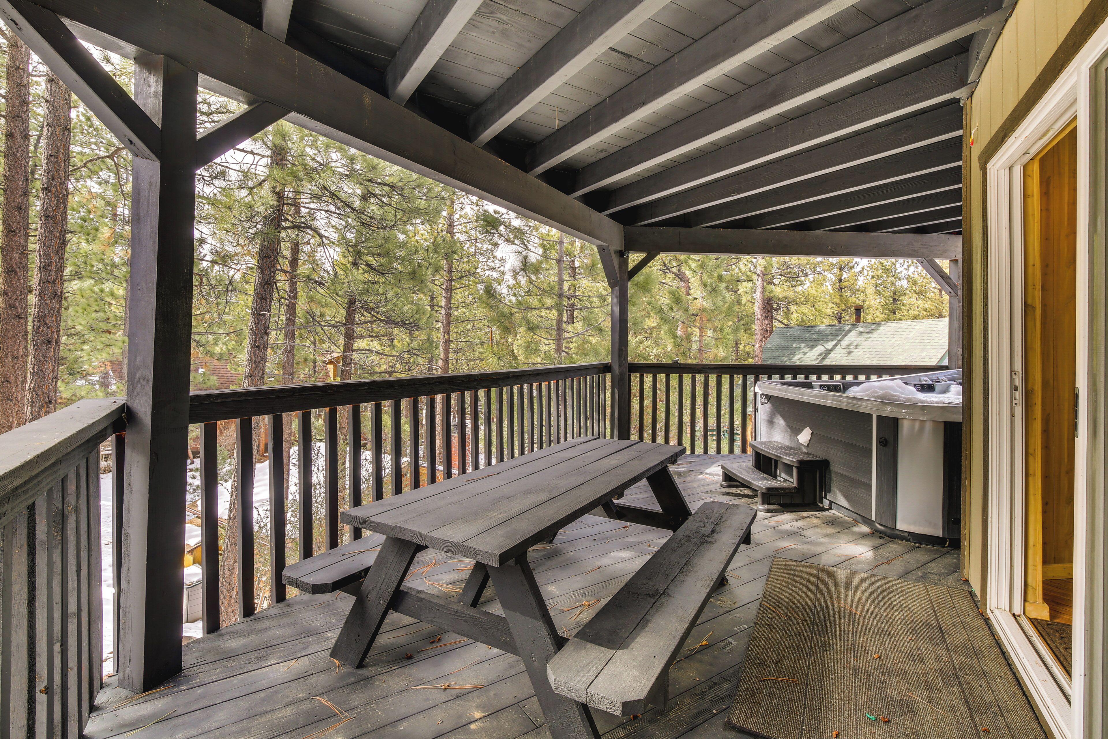 A covered outdoor area with a picnic table and grill, surrounded by trees.