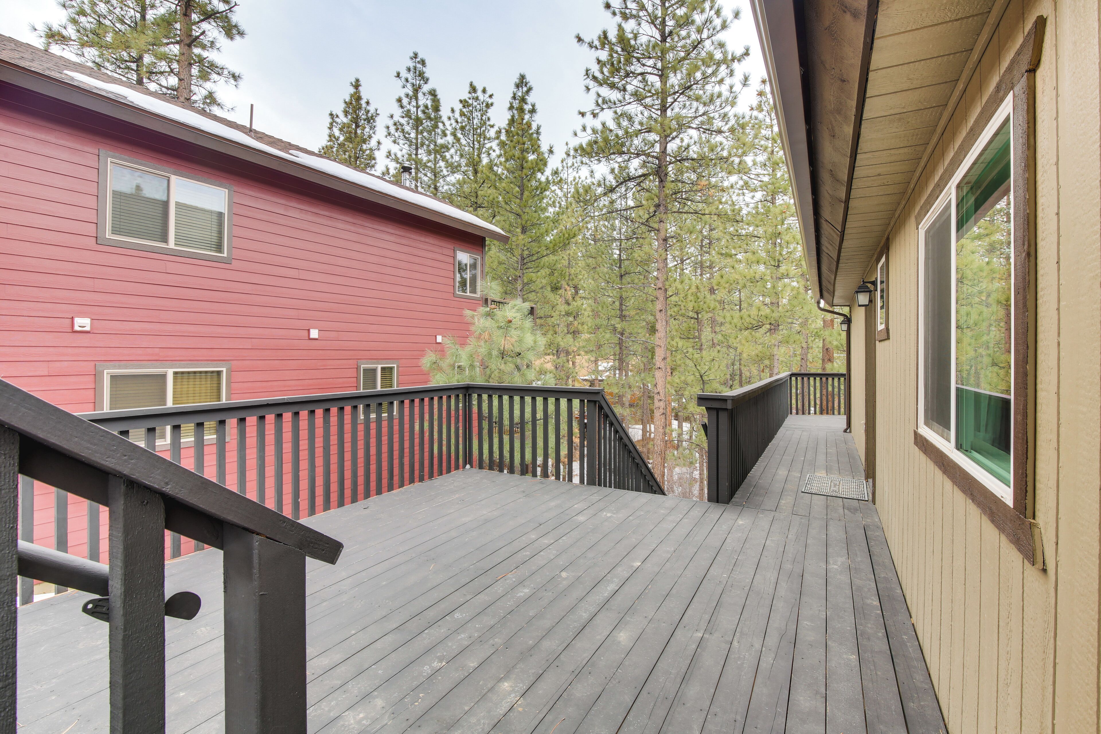 A wooden deck with a black railing, a red building in the background, and a view of trees.