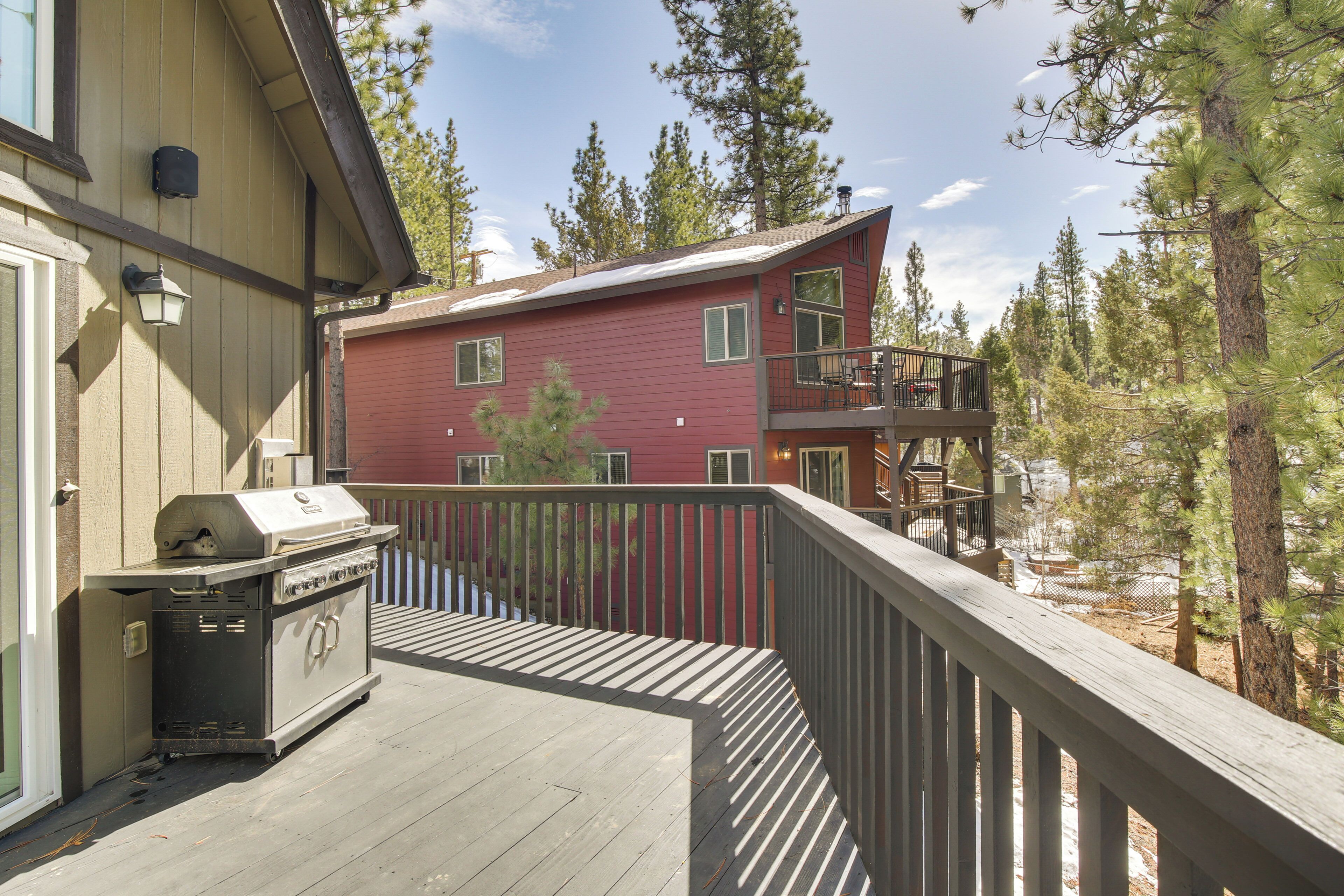 Une terrasse avec un barbecue, un bâtiment rouge doté d’un balcon, et une zone boisée en arrière-plan.