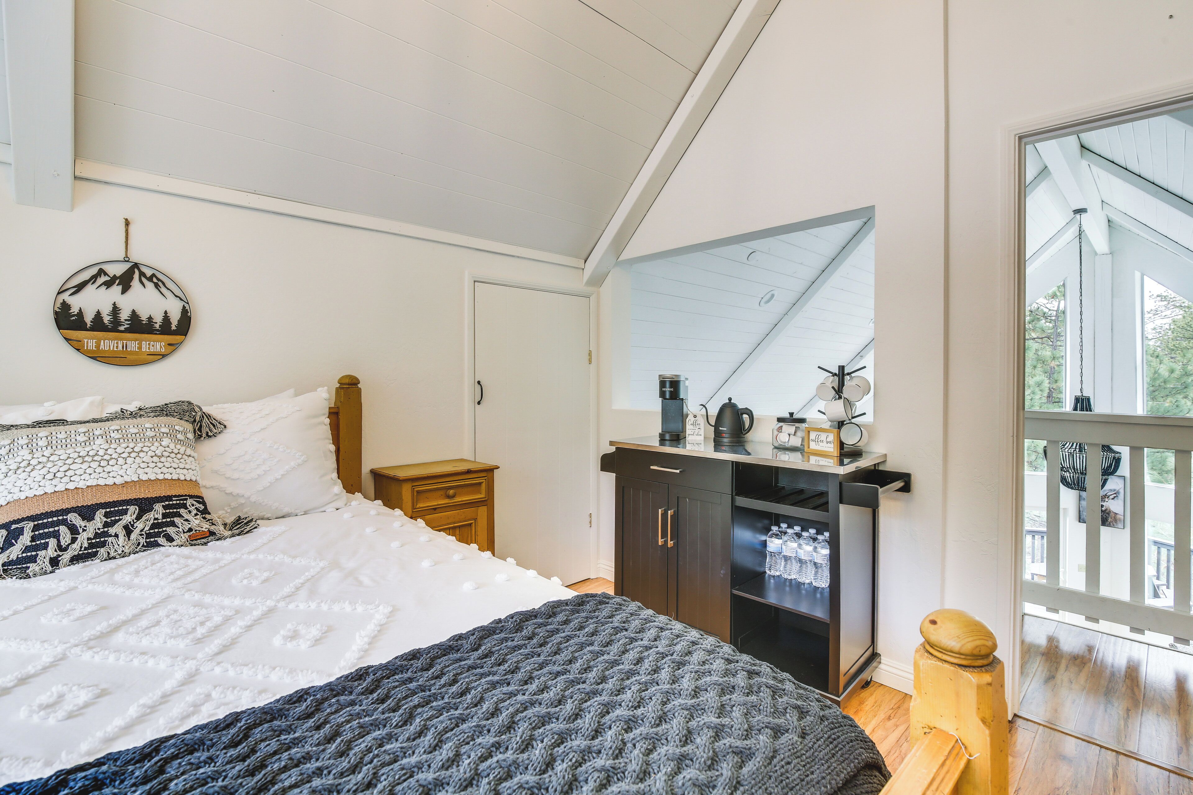 A bedroom with a bed, a dresser, a mirror, and a window with a view of the outdoors.