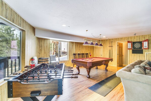 A room with a foosball table, pool table, and a sofa.