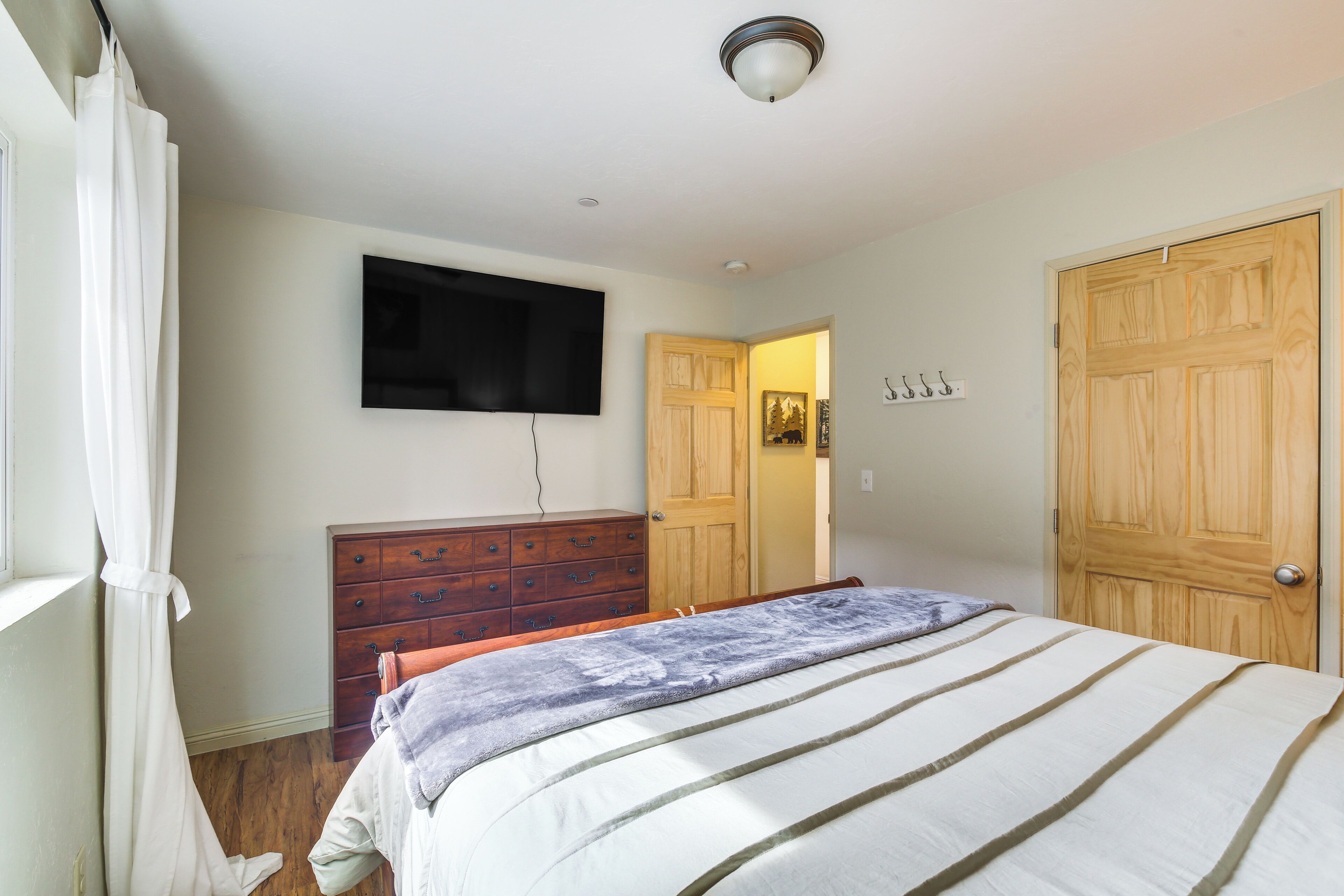 A bedroom with a bed, a dresser, a television mounted on the wall, and a wooden door.