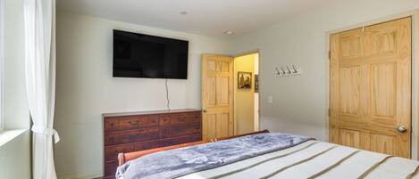 A bedroom with a bed, a dresser, a television mounted on the wall, and a wooden door.