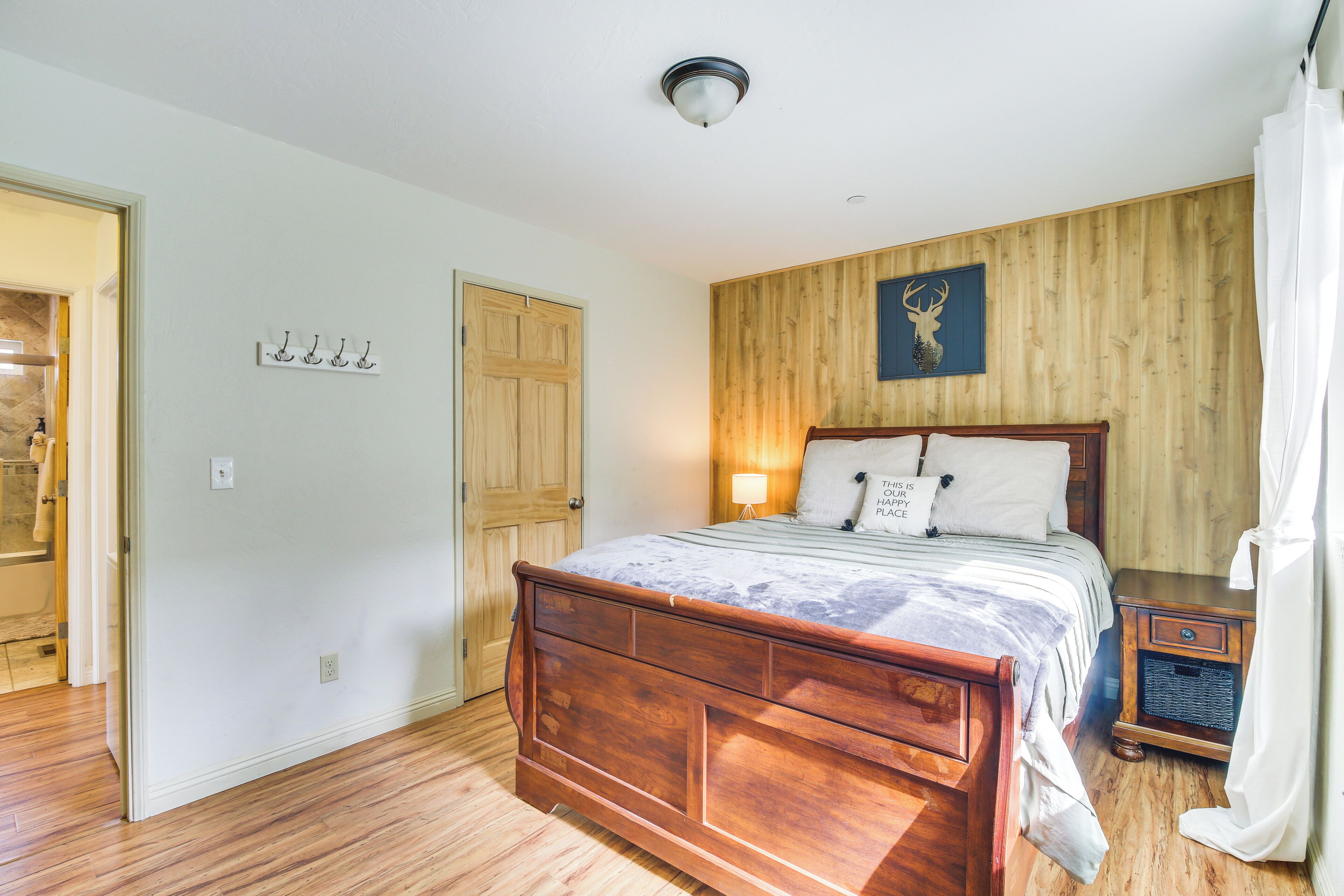 Un dormitorio con cama de madera, una mesita de noche, un panel de madera en la pared, una puerta y un aplique.