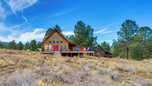 A large wooden cabin with a prominent front porch and multiple windows, surrounded by dry grassland and trees. - Mountain Home w/ Deck: 1 Mi to Angel Fire Resort! (Angel Fire)