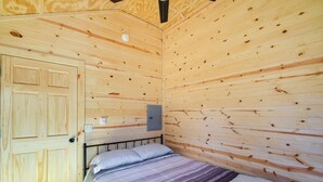 Une pièce aux murs lambrissés, avec un lit, une porte et un interrupteur sur le mur.