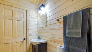 Une salle de bain aux murs lambrissés, équipée d’un lavabo, d’un miroir et d’un porte-serviettes.