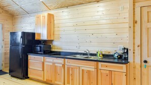 Une cuisine de taille réduite, avec des meubles de rangement en bois, un réfrigérateur noir, un four à micro-ondes et un évier.