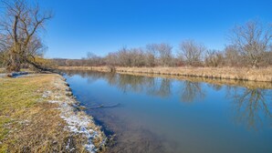 Une rivière paisible, bordée d’arbres sans feuilles et surplombée d’un ciel bleu clair.