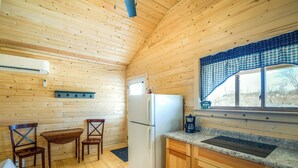 Una cocina compacta con paredes de madera, un refrigerador, una cafetera y una ventana con cortina a cuadros.