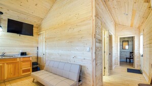 Interior de una cabaña de troncos con un sofá, armarios de madera, un televisor de pantalla plana y un comedor.