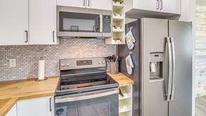 A modern kitchen with stainless steel appliances, white cabinets, and a brick backsplash.