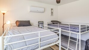 A room with bunk beds, a ceiling fan, an air conditioner, a wall-mounted mirror, and a lamp.