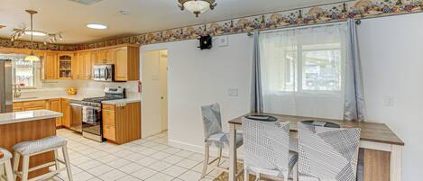 A modern kitchen with wooden cabinets, a central island, and a dining area with patterned chairs.