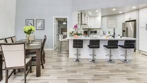 Una cocina moderna con armarios blancos, una isla central con taburetes y un comedor con mesa y sillas de madera.