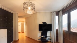 A hotel room with a wooden floor, a TV on a stand, a bed, a ceiling light fixture, and a view of the outside. - Ekain - baskeyrentals (Zestoa)