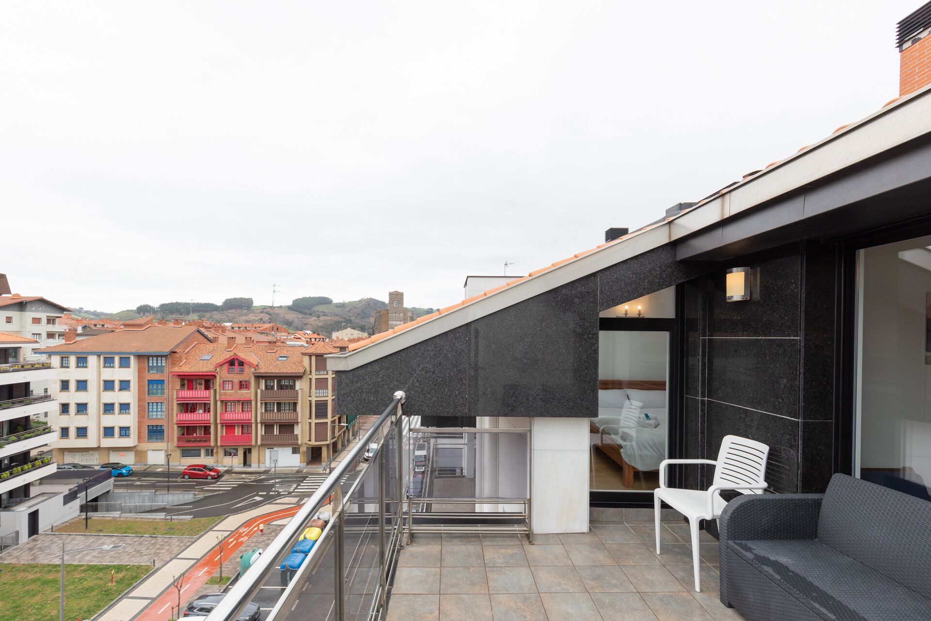 Een modern gebouw met balkon, glazen deur en een zithoek met stoel en bank.