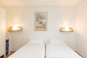 A room with two single beds, a framed poster on the wall, and wall-mounted lights. - Telmo - baskeyrentals (Zumaia)