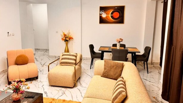 A modern living room with a sofa, armchairs, a coffee table, and a dining area with a table and chairs. - Everluxe Residence  (Abidjan)