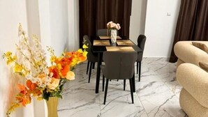 A dining area with a marble floor, a dining table with chairs, and a vase with flowers on the side. - Everluxe Residence  (Abidjan)