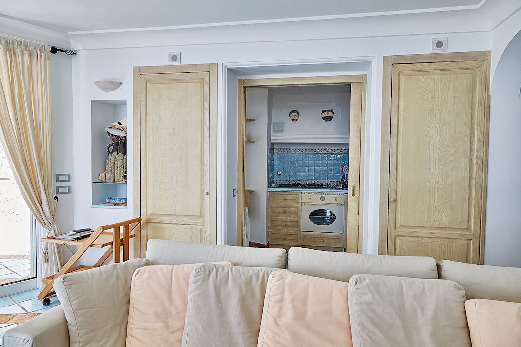 Een kamer met een beige bank, een houten bureau en een kast met een blauwe tegelachtergrond.
