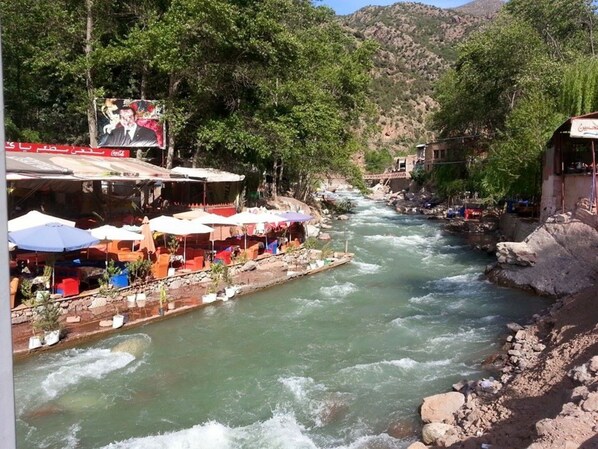Un río con un bote atracado a la izquierda, rodeado de terrazas al aire libre con sombrillas.