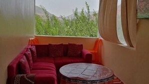 Una habitación con un sofá rojo, una mesita redonda y vistas a la vegetación y montañas a través de una ventana.